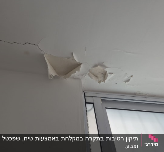 קיר עם סדקים ותקרה מתקלפת ליד חלון